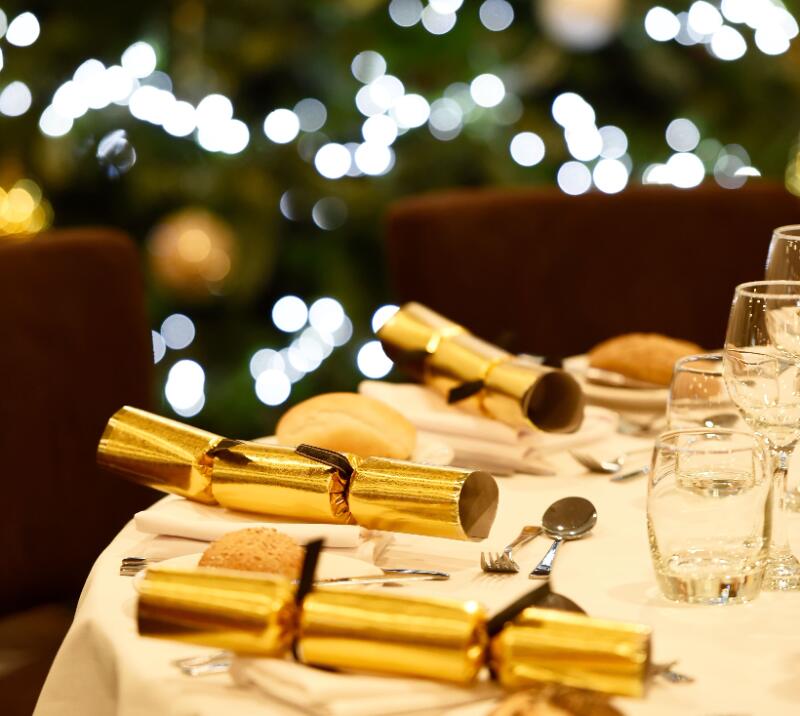 A festive dining table with Christmas crackers, in front of a twinkly Christmas tree