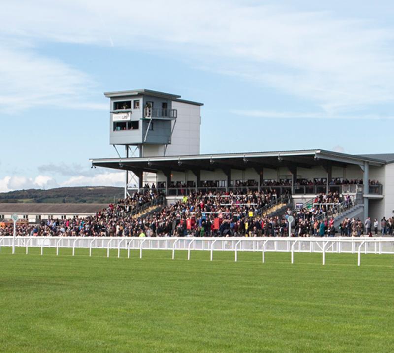 Crowds watching racing from the grandstand at Ffos Las Racecourse.